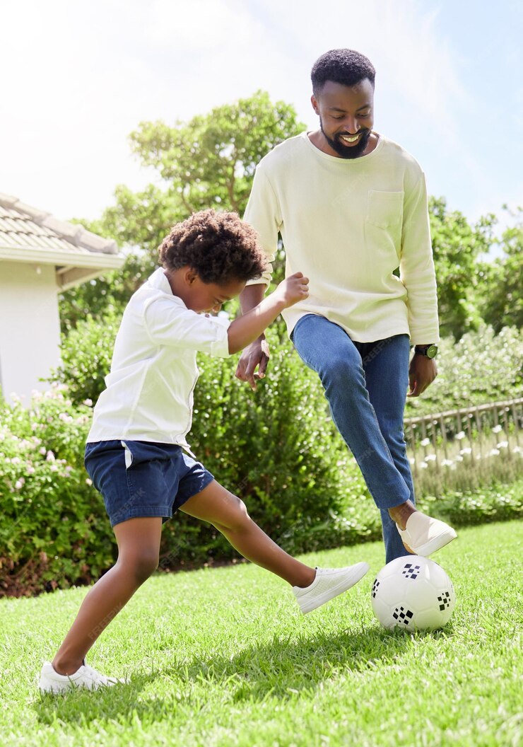 Homme noir et fils en train de créer des liens avec un ballon de football dans l'arrière-cour d'une maison de jardin ou dans un parc gazonné pour un match de jeu amusant et une compétition. Sourire heureux et football pour le père et le garçon lors d'exercices de remise en forme et d'entraînement